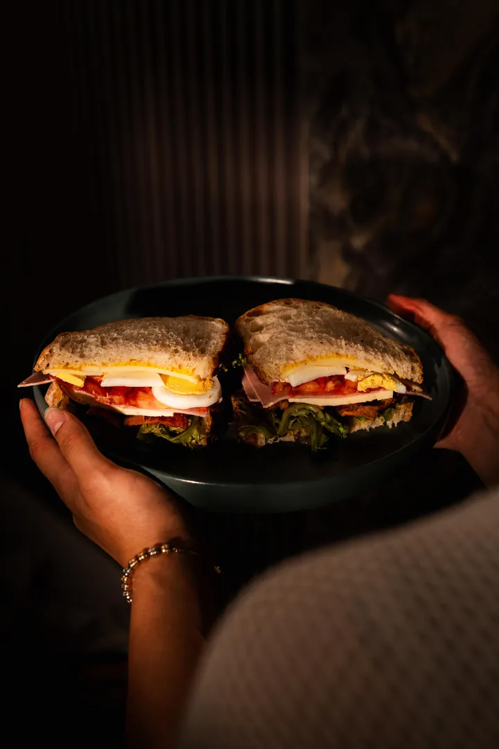 Sándwich club cortado a la mitad servido en plato oscuro